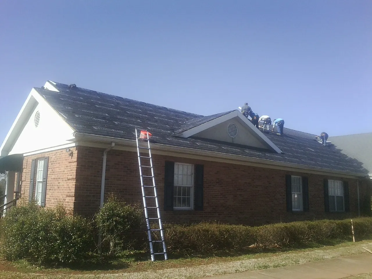 Crew tearing shingles off a brick ranch roof with a ladder set — Metal Roof Repair work by our crew in Sutherlin