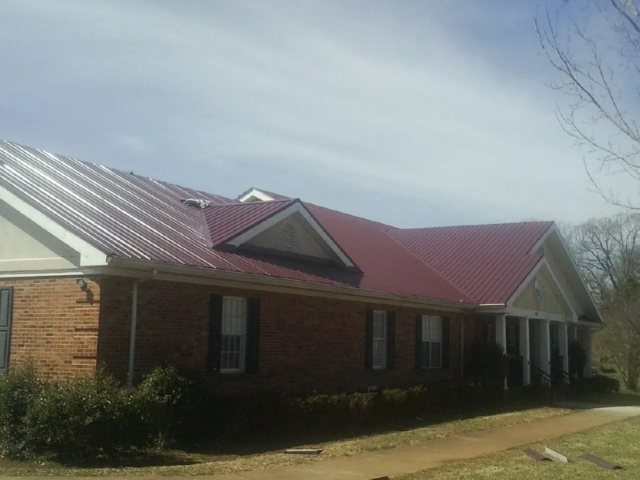 Red metal roof with gabled entries on a long brick building, from a Hail Damage Roof Repair job in Sutherlin