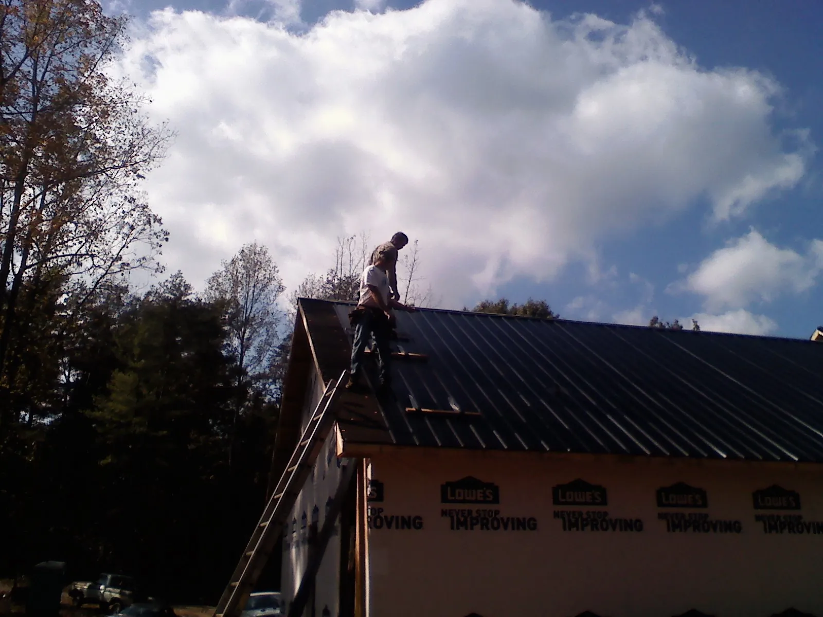Roofer fastening dark metal panels high against a cloudy sky, from a Roof Inspection job in Sutherlin