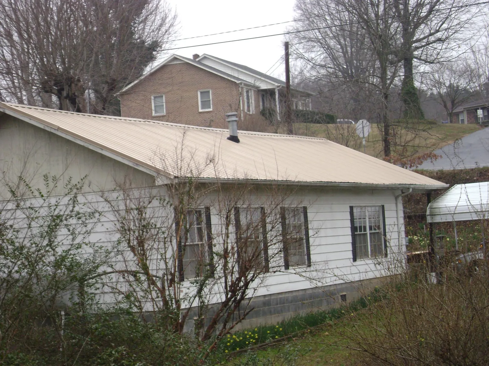 Tan metal roof on a white sided house set into a hillside — Commercial Roofing by Roofing Brothers in Sutherlin